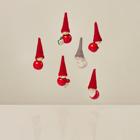 Six small hanging Christmas elf ornaments in red and gray felt, arranged against a plain warm beige background.